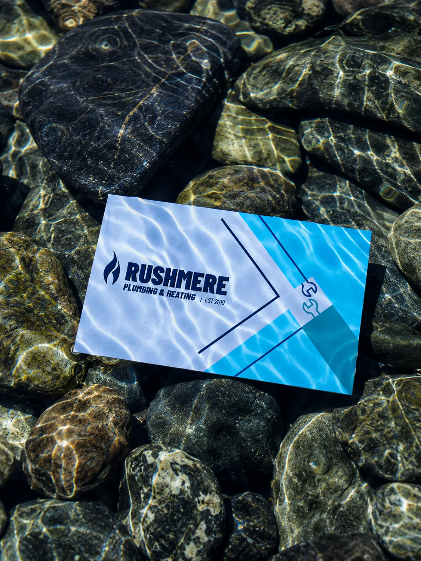 Rushmere business card resting on wet river stones under shallow water