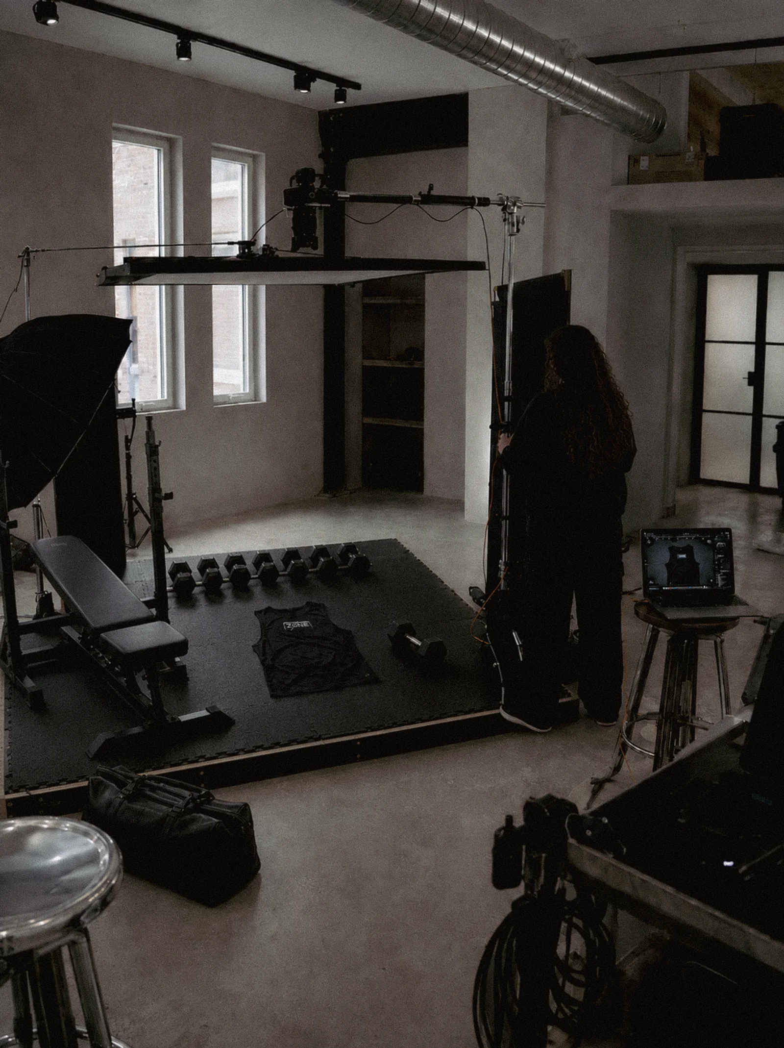 Studio set with an overhead camera rig above a black training platform, a Zone vest laid flat between dumbbells