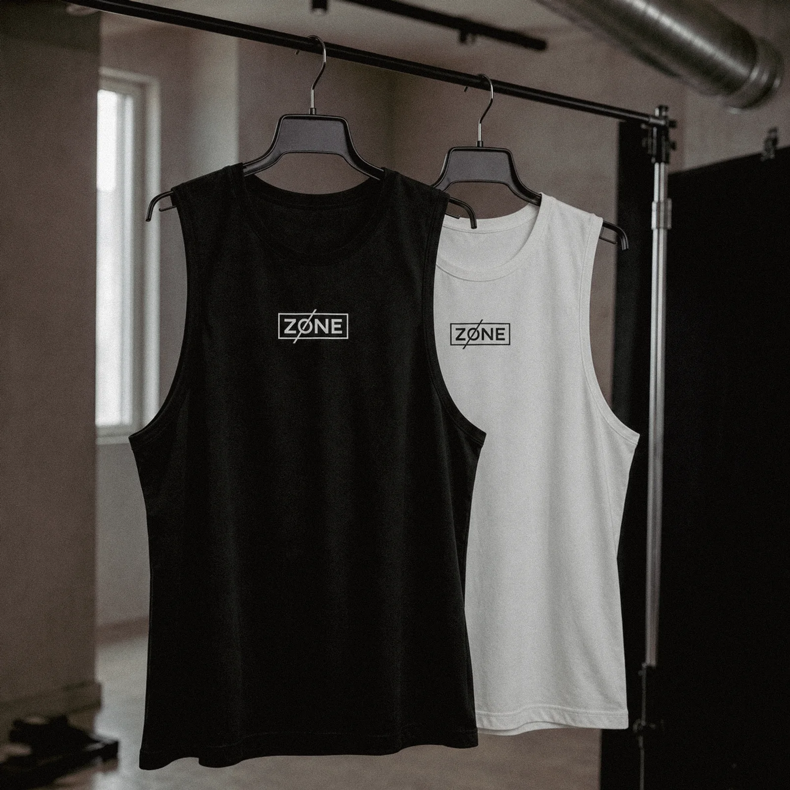 Black and white Zone training vests hanging side by side, each carrying the boxed wordmark at the chest